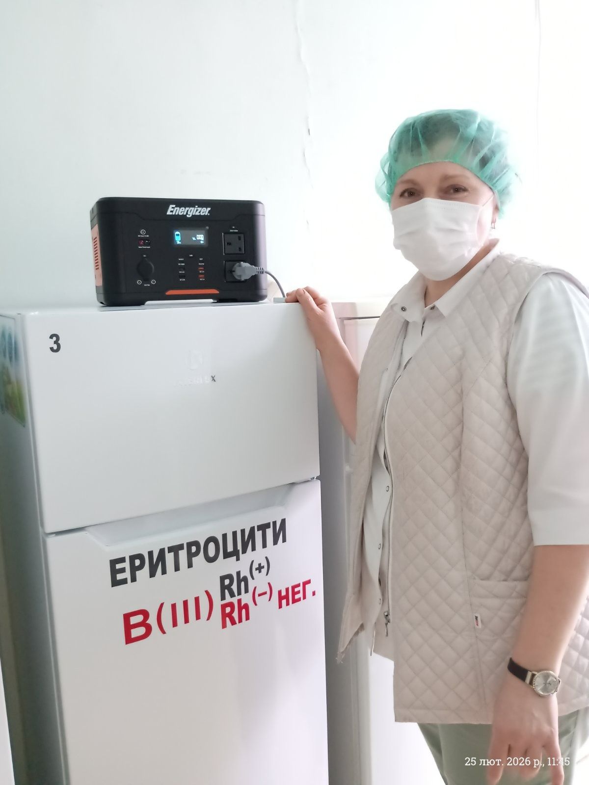 Портативна зарядна станція Energizer стоїть на холодильнику банку крові, підключена до нього кабелем. На холодильнику маркування «Еритроцити B(III) Rh(+), Rh(−) нег.». Поруч стоїть медпрацівниця в медичній формі та шапочці.